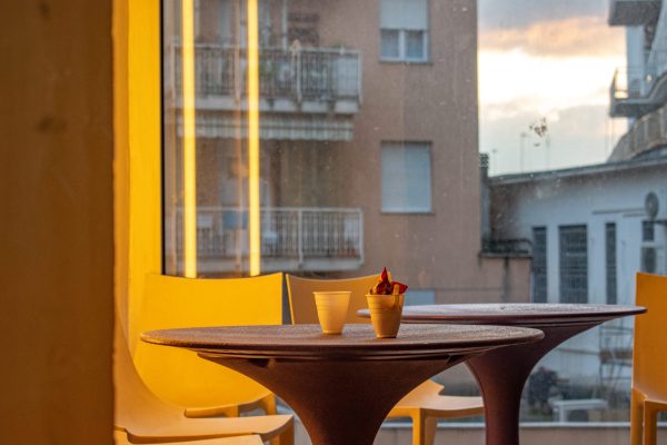 Area ristoro, tavolini e sedie con vista sugli edifici di sera, e bicchierini di caffè bevuti lasciati sul tavolo